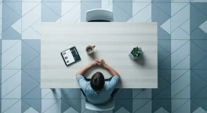 Decoding Tomorrow: Unpacking the Internet's Evolving Landscape Aerial view of a person at a dining table, illustrating the integration of digital devices like a tablet into daily life, surrounded by geometric floor patterns.