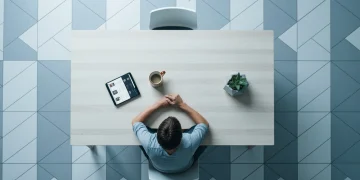 Aerial view of a person at a dining table, illustrating the integration of digital devices like a tablet into daily life, surrounded by geometric floor patterns.