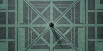 A solitary person viewed from above on a mosaic plaza, with subtle green digital data streams emanating, symbolizing invisible data collection.